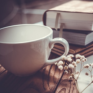 Books, flowers, white cup and opened diary on wooden table